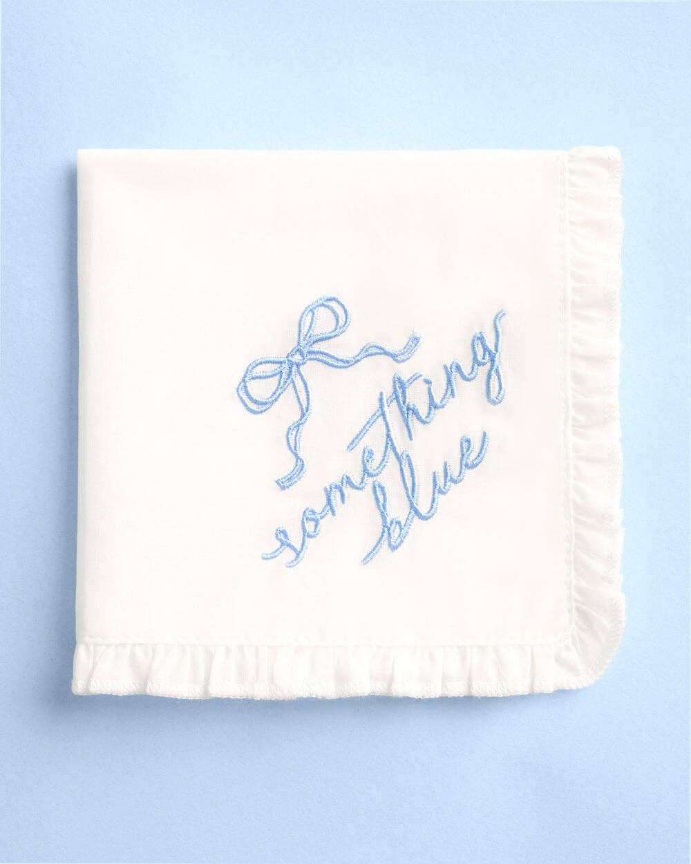 White ruffled handkerchief embroidered with blue something blue script and bow