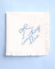 White ruffled handkerchief embroidered with blue something blue script and bow