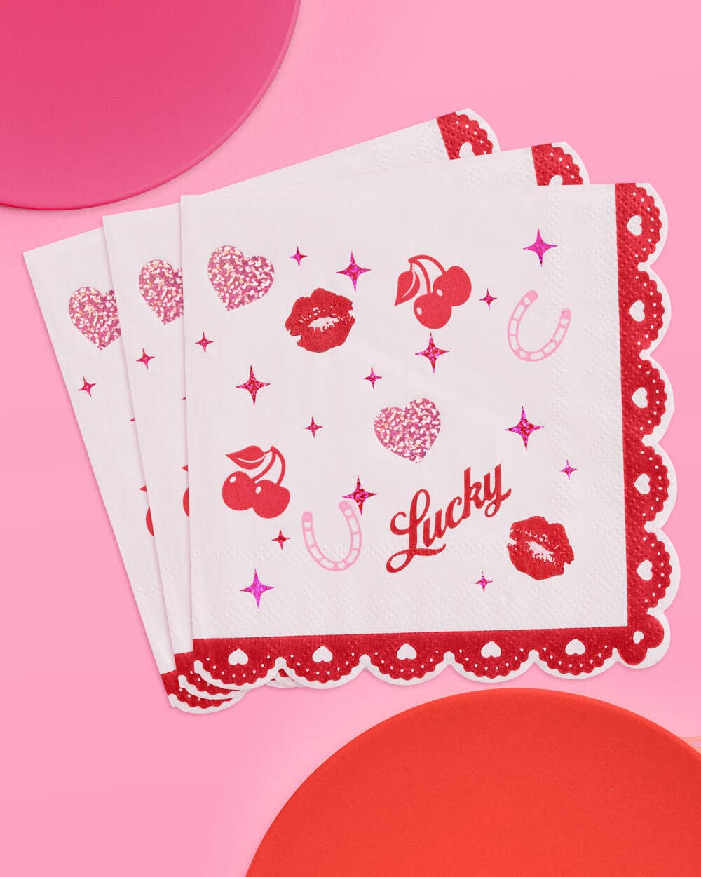 Scalloped edge cocktail napkins printed with cherries, lips, and hearts in pink foil